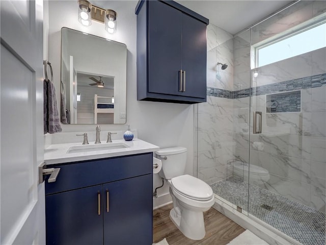 bathroom featuring a stall shower, toilet, ceiling fan, wood finished floors, and vanity