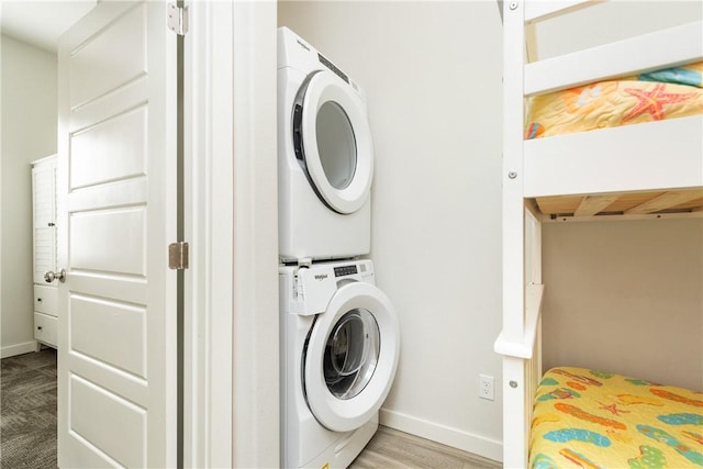 washroom featuring stacked washer / dryer, laundry area, and baseboards