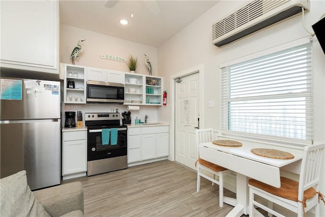 kitchen featuring open shelves, a wall mounted AC, appliances with stainless steel finishes, light wood-style floors, and a sink