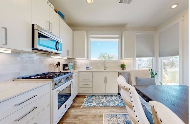 kitchen with white cabinets, sink, tasteful backsplash, light wood-type flooring, and appliances with stainless steel finishes