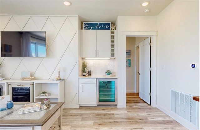 bar with wine cooler, white cabinetry, backsplash, and light wood-type flooring