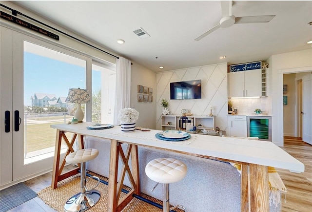 kitchen with french doors, white cabinetry, light wood-type flooring, a breakfast bar area, and beverage cooler