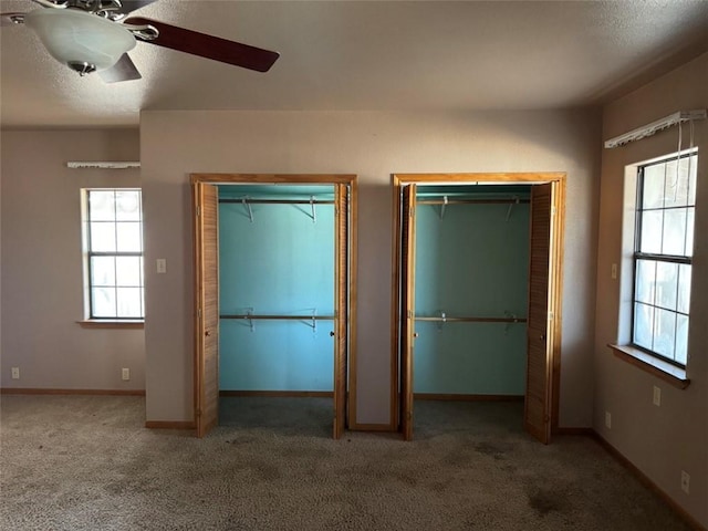 unfurnished bedroom featuring multiple closets, dark colored carpet, a textured ceiling, and ceiling fan