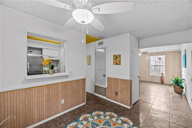 interior space with ceiling fan, a textured ceiling, a wainscoted wall, visible vents, and stainless steel fridge