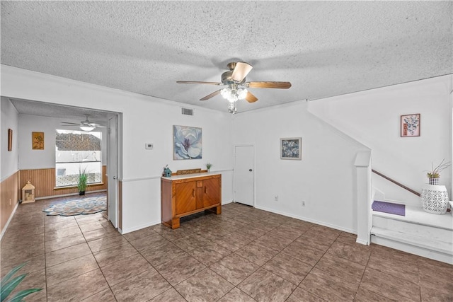 interior space featuring ceiling fan, visible vents, a textured ceiling, and wainscoting