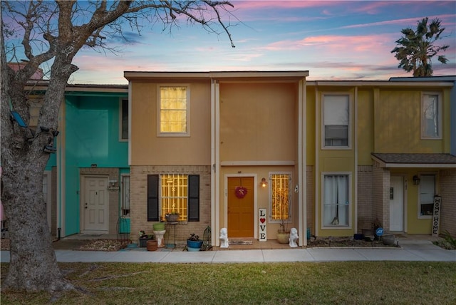 townhome / multi-family property featuring brick siding, a front lawn, and stucco siding