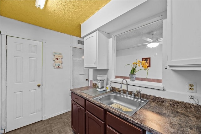 kitchen with a textured ceiling, dark countertops, a sink, and white cabinets