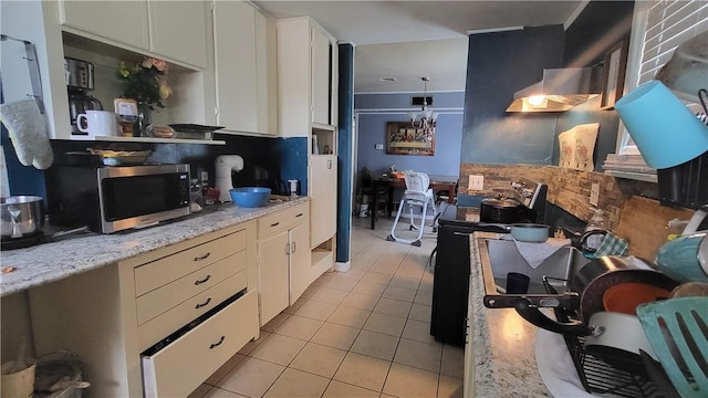 kitchen with light stone counters, range with electric stovetop, stainless steel microwave, white cabinetry, and extractor fan