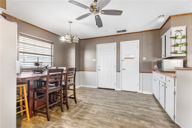 dining room featuring ceiling fan with notable chandelier, a textured ceiling, light wood-type flooring, and ornamental molding