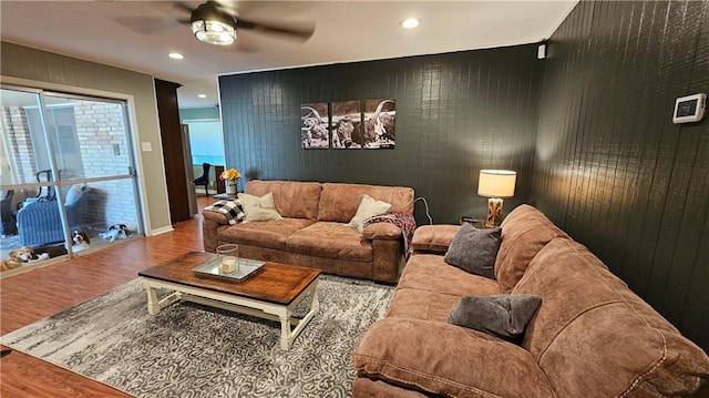 living room featuring wood walls, wood-type flooring, and ceiling fan