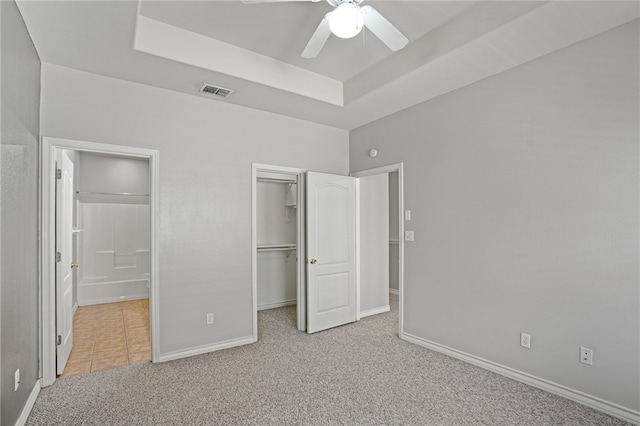 unfurnished bedroom featuring a closet, a walk in closet, a raised ceiling, light colored carpet, and ceiling fan