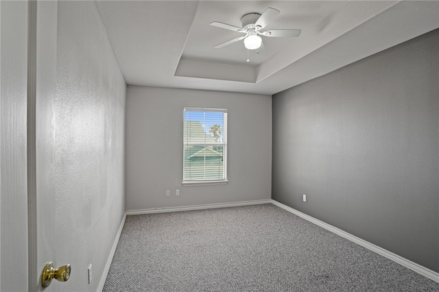 carpeted spare room featuring ceiling fan and a tray ceiling