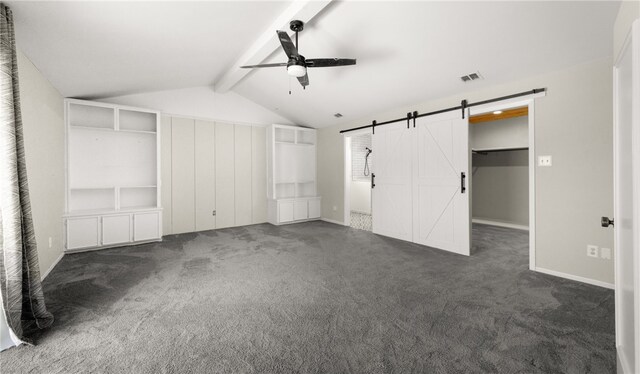 unfurnished bedroom featuring ceiling fan, a walk in closet, dark carpet, a barn door, and lofted ceiling with beams