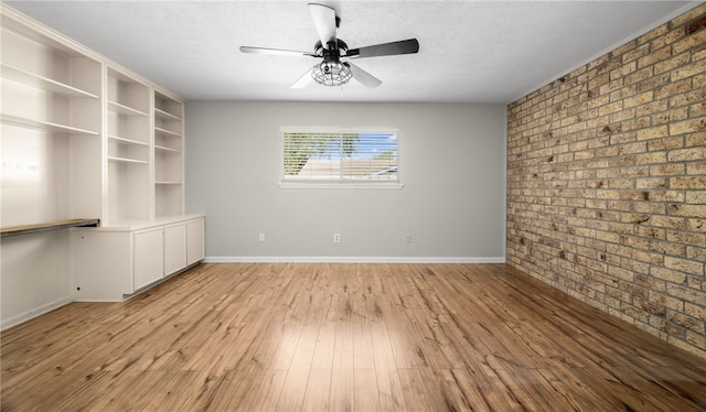 unfurnished room with ceiling fan, light hardwood / wood-style floors, and brick wall