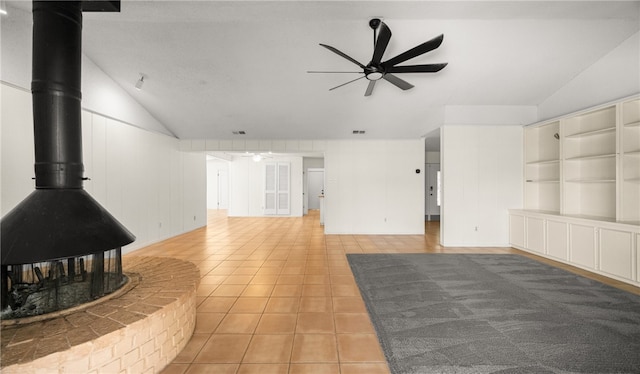 unfurnished living room featuring ceiling fan, light tile patterned floors, a wood stove, and vaulted ceiling