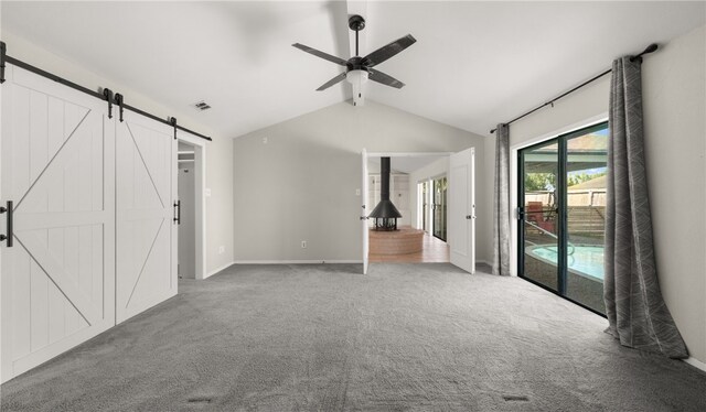 unfurnished living room featuring a barn door, carpet, vaulted ceiling, and ceiling fan