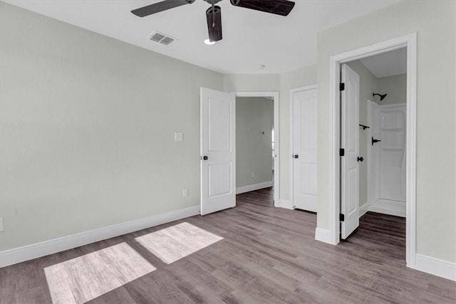 unfurnished bedroom featuring a ceiling fan, visible vents, baseboards, and wood finished floors