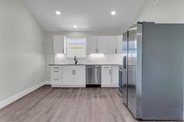 kitchen featuring appliances with stainless steel finishes, light wood-style floors, a sink, and decorative backsplash