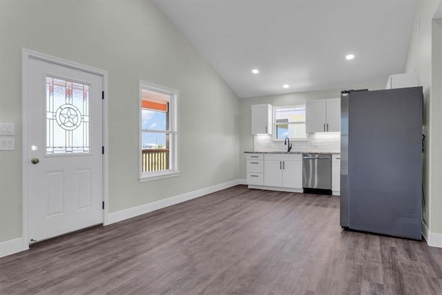 kitchen featuring lofted ceiling, stainless steel appliances, a sink, white cabinets, and decorative backsplash