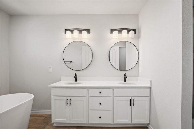 bathroom with a sink, a soaking tub, wood finished floors, and double vanity