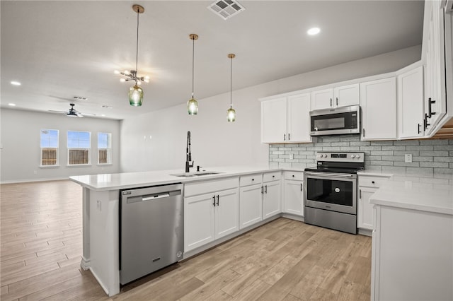 kitchen featuring visible vents, a peninsula, a sink, stainless steel appliances, and backsplash