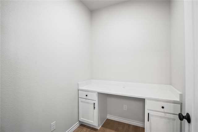 unfurnished office with wood finished floors, built in desk, and baseboards