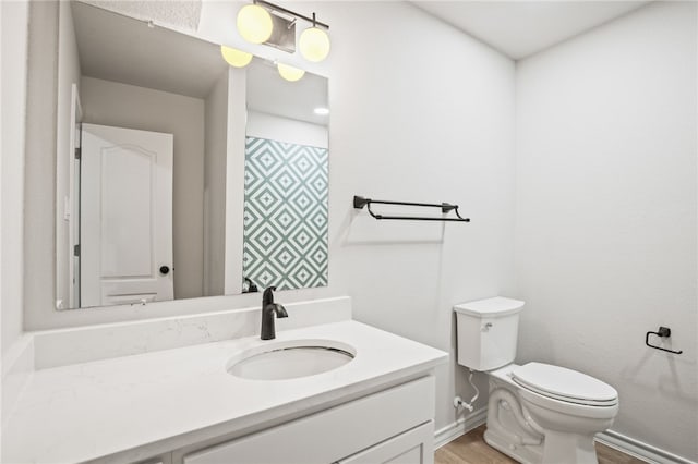 bathroom featuring baseboards, toilet, wood finished floors, and vanity