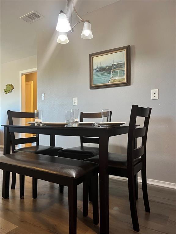 dining room featuring a notable chandelier, baseboards, visible vents, and wood finished floors