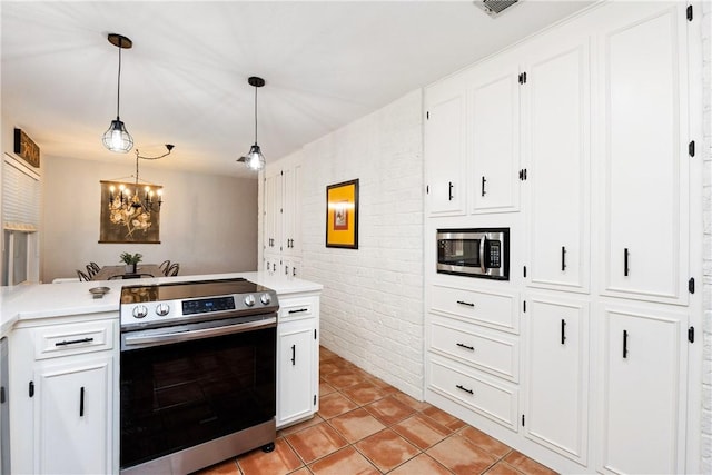 kitchen featuring light tile patterned floors, appliances with stainless steel finishes, white cabinetry, hanging light fixtures, and brick wall