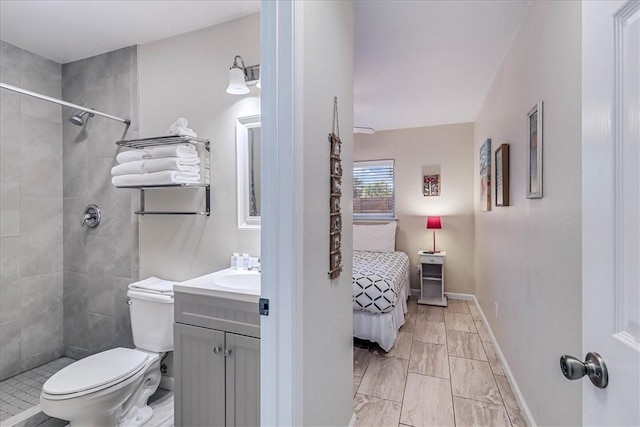 ensuite bathroom with toilet, ensuite bathroom, a tile shower, vanity, and baseboards