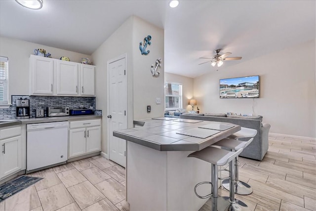 kitchen with tile countertops, backsplash, open floor plan, white dishwasher, and a kitchen bar