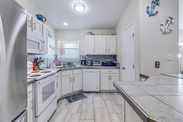 kitchen with a sink, white appliances, white cabinets, and backsplash