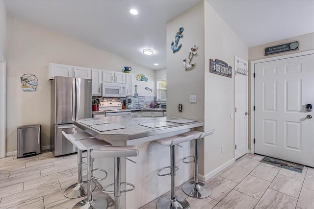 kitchen with white microwave, stove, a breakfast bar, freestanding refrigerator, and backsplash