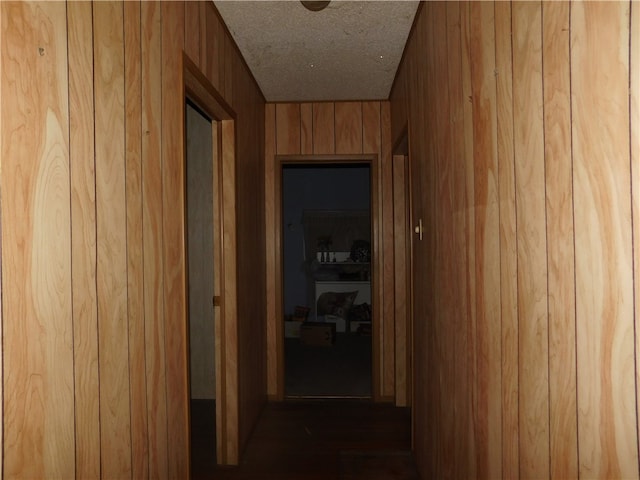 corridor with wood walls, a textured ceiling, and dark wood-type flooring