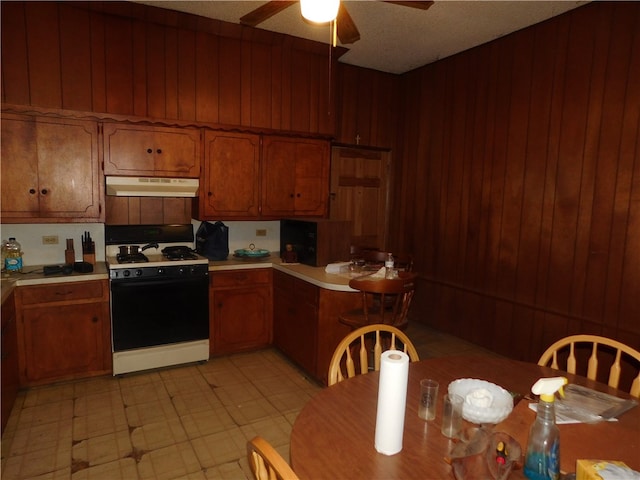 kitchen with ceiling fan, wooden walls, a textured ceiling, and white gas range oven