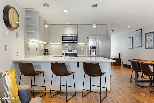 kitchen with dark wood-style floors, light countertops, appliances with stainless steel finishes, a sink, and a peninsula