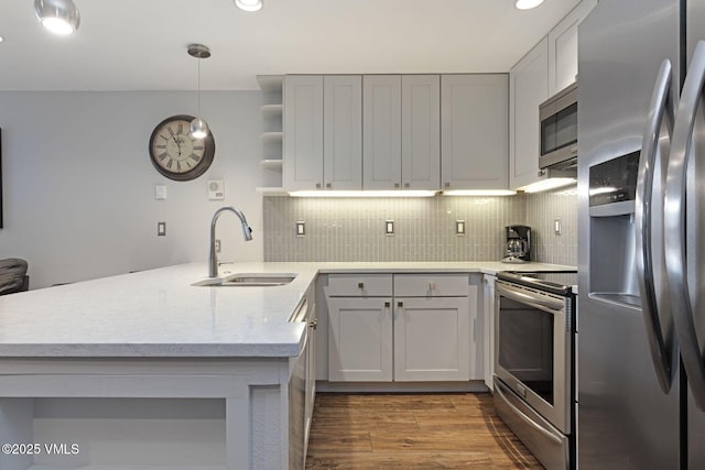 kitchen with a peninsula, wood finished floors, a sink, appliances with stainless steel finishes, and backsplash