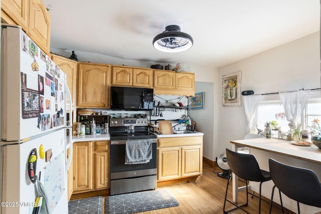 kitchen featuring black microwave, wood finished floors, light countertops, freestanding refrigerator, and stainless steel electric range oven