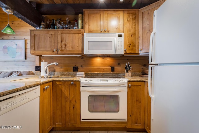 kitchen with white appliances, brown cabinetry, light stone counters, wood walls, and a sink