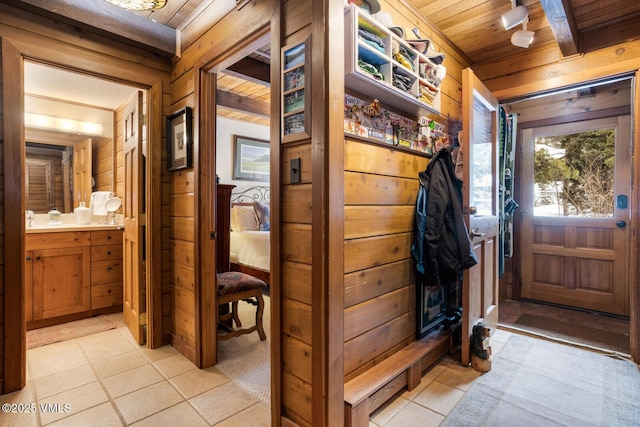 mudroom with wooden ceiling, wooden walls, light tile patterned floors, and beam ceiling