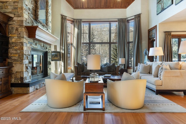 living room featuring wood ceiling, a towering ceiling, a stone fireplace, and light hardwood / wood-style floors