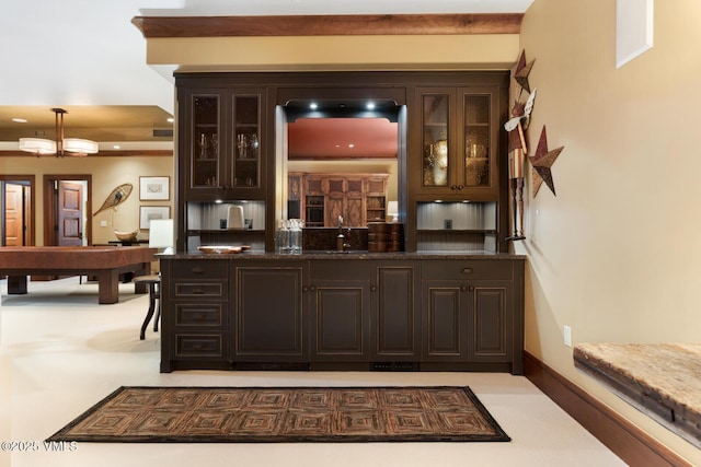 bar with sink, decorative light fixtures, dark brown cabinets, and dark stone counters