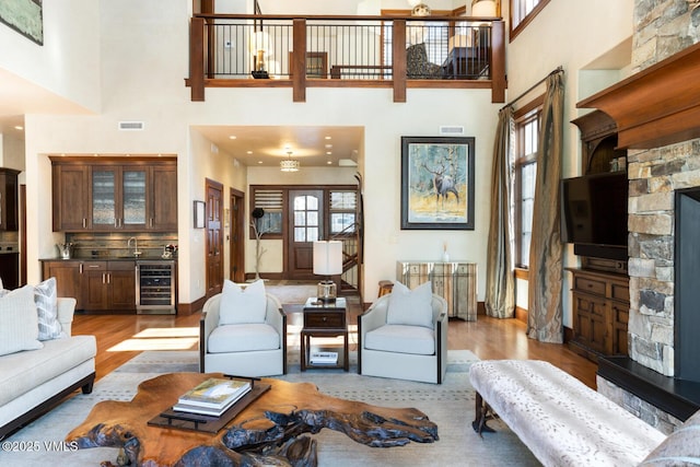 living room with a stone fireplace, a towering ceiling, wine cooler, and light wood-type flooring