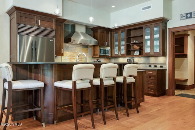 153 Village Walk, Beaver Creek, CO 81620 - kitchen with wall chimney range hood, appliances with stainless steel finishes, open shelves, light wood-type flooring, and decorative light fixtures