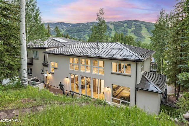784 Potato Patch Dr Unit W, Vail, CO 81657 - back of property at dusk with stucco siding, a standing seam roof, a mountain view, and a metal roof