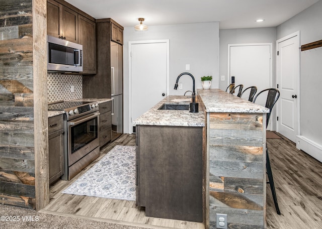 3971 Big Horn Rd Unit 7-N, Vail, CO 81657 - kitchen with stainless steel appliances, dark brown cabinets, light wood-type flooring, a center island with sink, and light stone counters