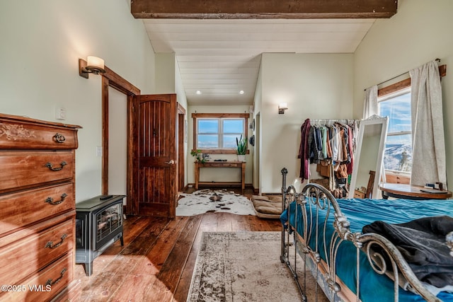 bedroom featuring a wood stove, lofted ceiling with beams, and hardwood / wood-style floors