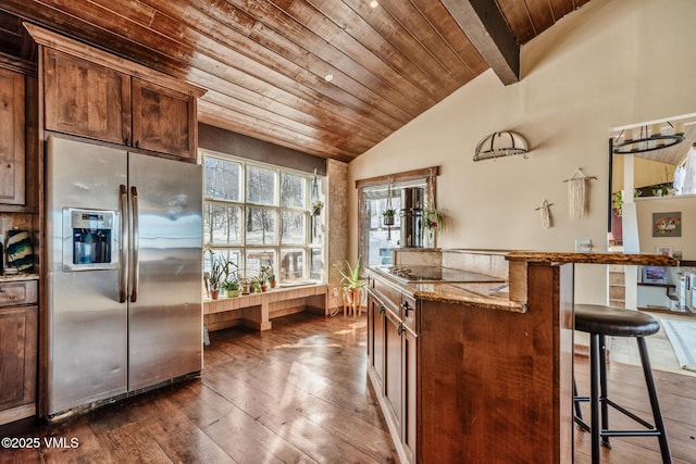 kitchen featuring stainless steel fridge, lofted ceiling with beams, wooden ceiling, light stone countertops, and a kitchen bar