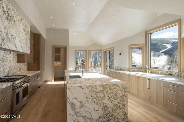 kitchen with range with two ovens, light wood finished floors, a sink, light stone countertops, and a large island with sink