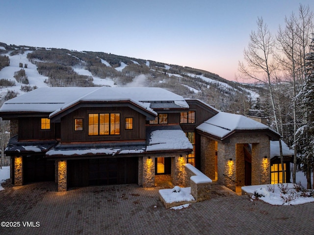 view of front facade with an attached garage, stone siding, a mountain view, and decorative driveway